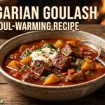 A steaming bowl of rich red Hungarian Goulash served in a cast iron pot with sour cream